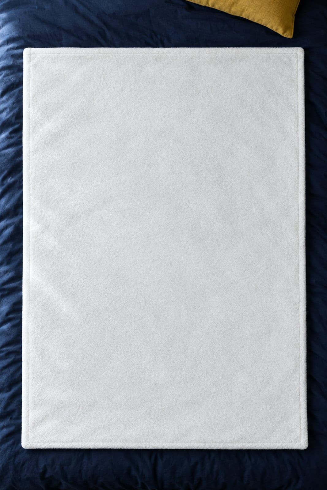 An oxblood fleece throw with a crest at its centre, on navy bedding